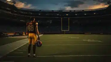NFL wide receiver in burgundy uniform standing alone on empty football field at dusk