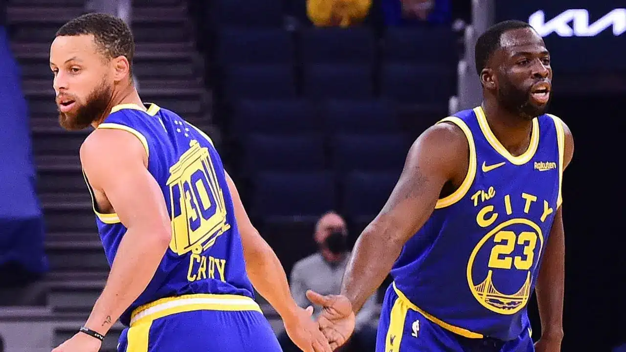 Stephen Curry and Draymond Green of the Golden State Warriors in blue and gold uniforms on the court.