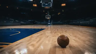 Empty Warriors basketball court at night with lone basketball, conveying defeat and accountability