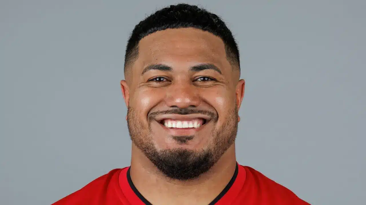 Headshot of Vita Vea smiling, wearing a red Tampa Bay Buccaneers jersey against a grey background