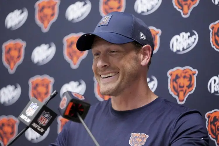 Ben Johnson smiling during a press conference in front of a Chicago Bears branded backdrop