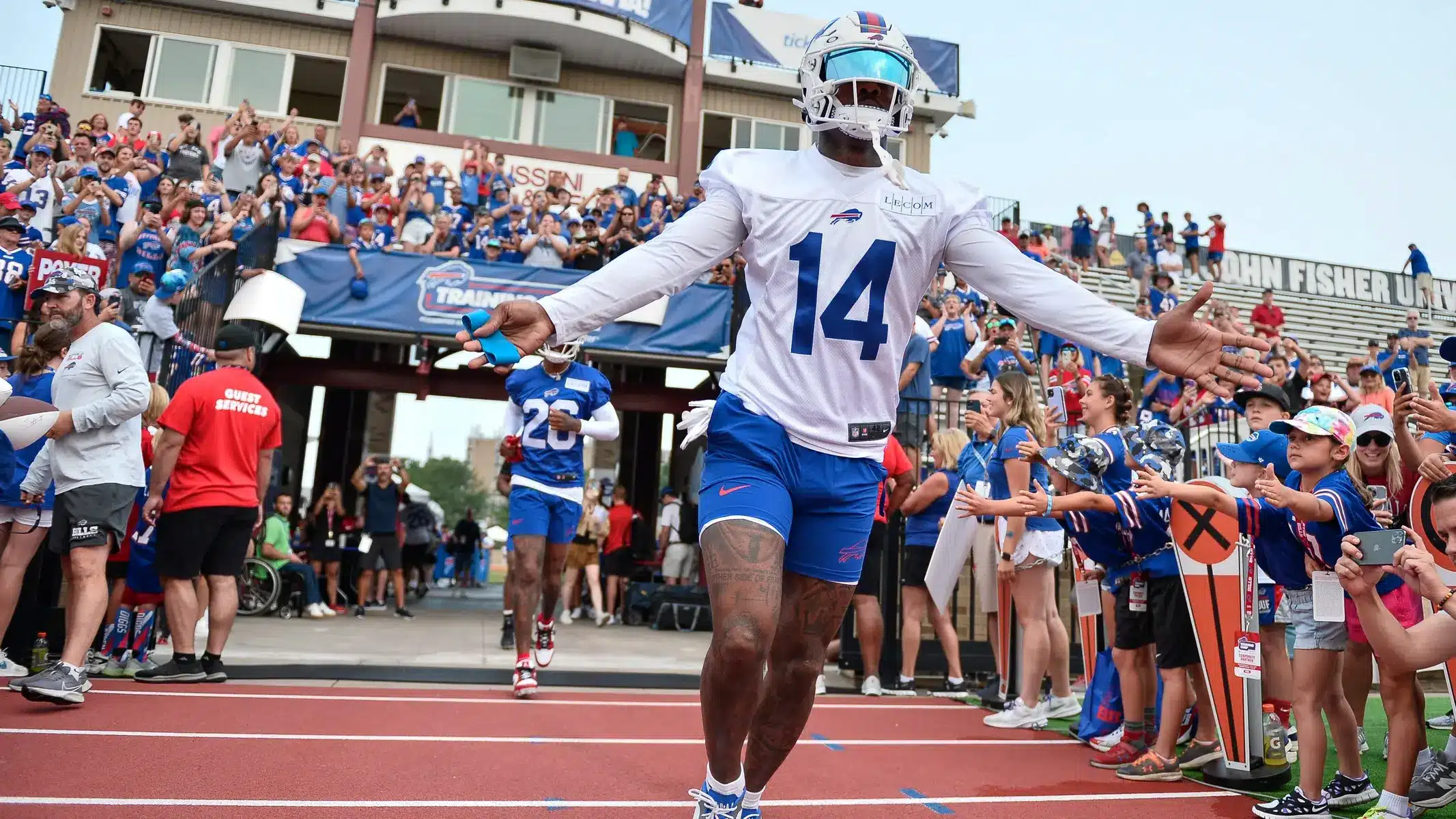 Buffalo Bills players in white practice gear walking toward cheering fans at training camp.