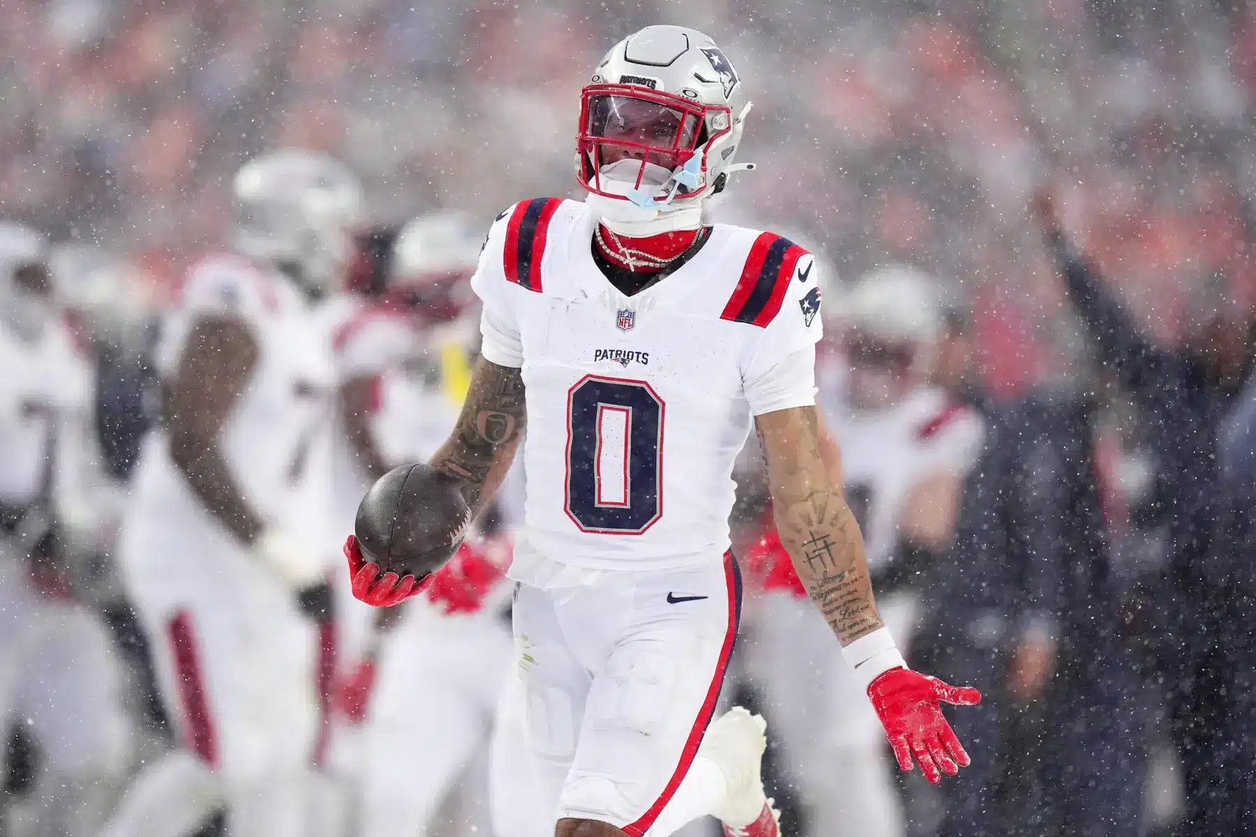 Christian Gonzalez of the New England Patriots wearing number 0 and holding a football in the snow