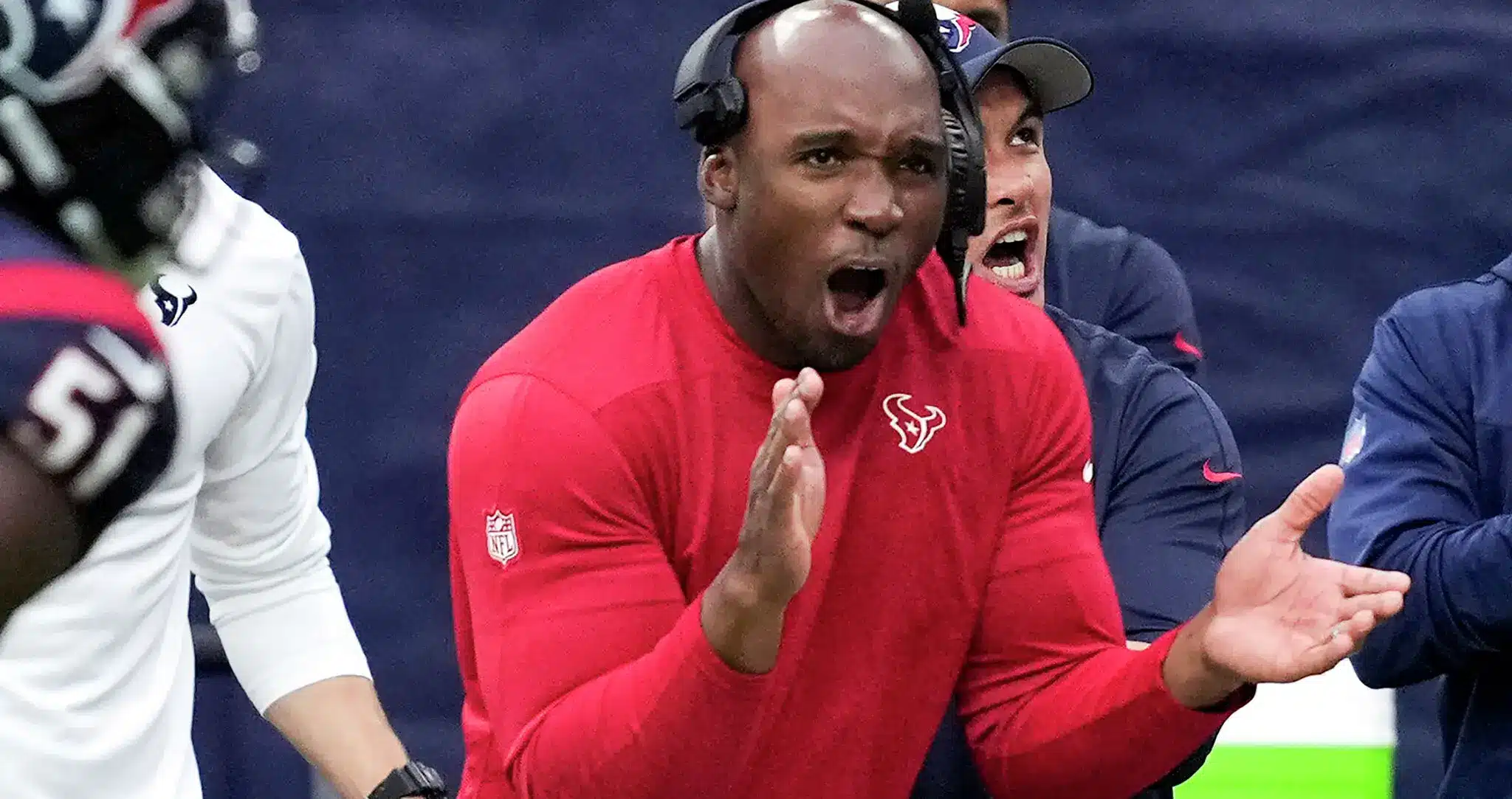 Houston Texans head coach DeMeco Ryans wearing a red pullover and headset, shouting on the sideline.