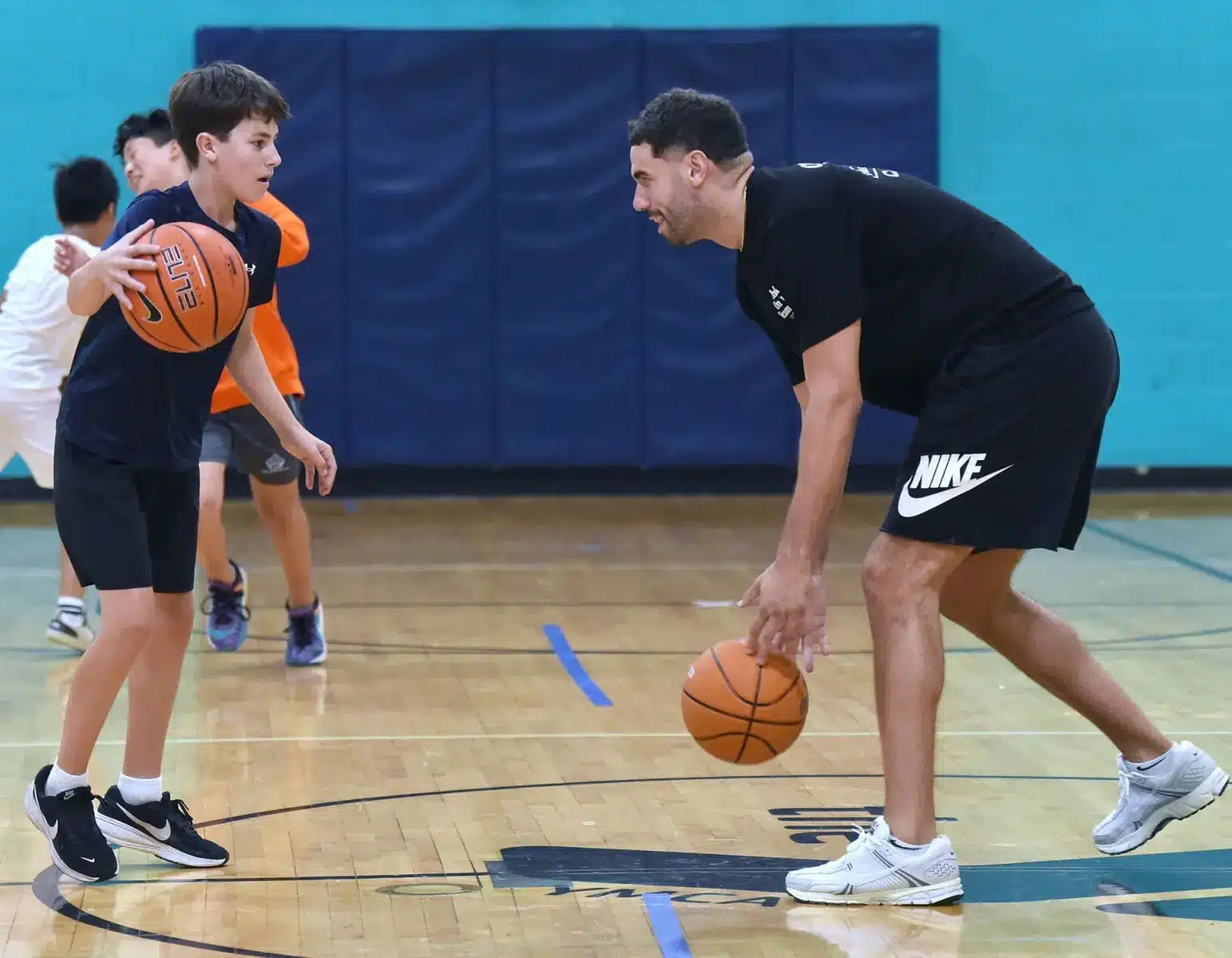 Georges Niang dribbling a basketball while coaching a youth player on an indoor court