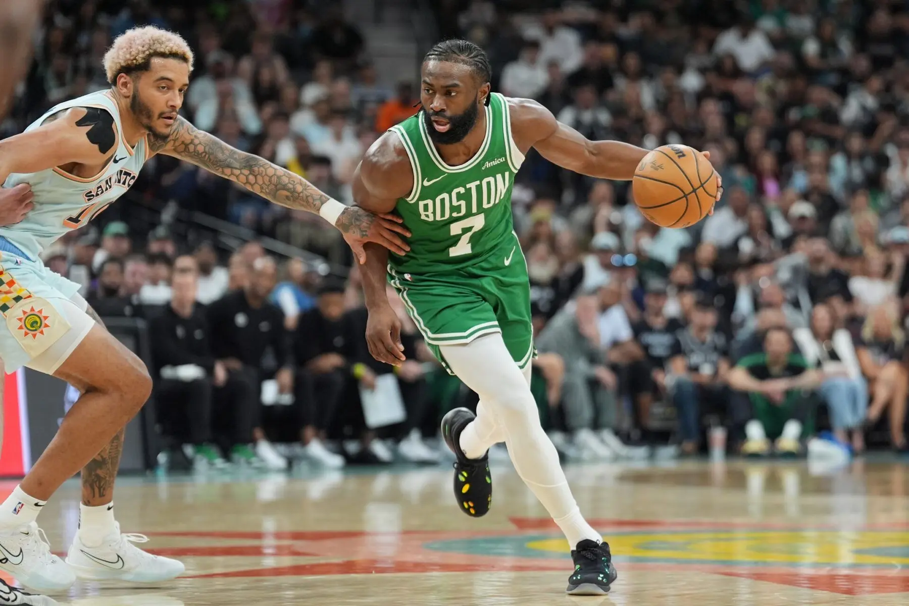 Jaylen Brown of the Boston Celtics dribbles a basketball while being guarded by a San Antonio Spurs player.