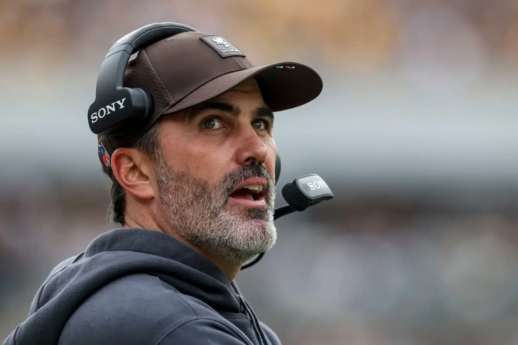 Close-up portrait of Kevin Stefanski wearing a brown cap and Sony headset on the sidelines