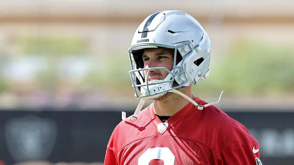A football player wearing a silver Las Vegas Raiders helmet and a red practice jersey