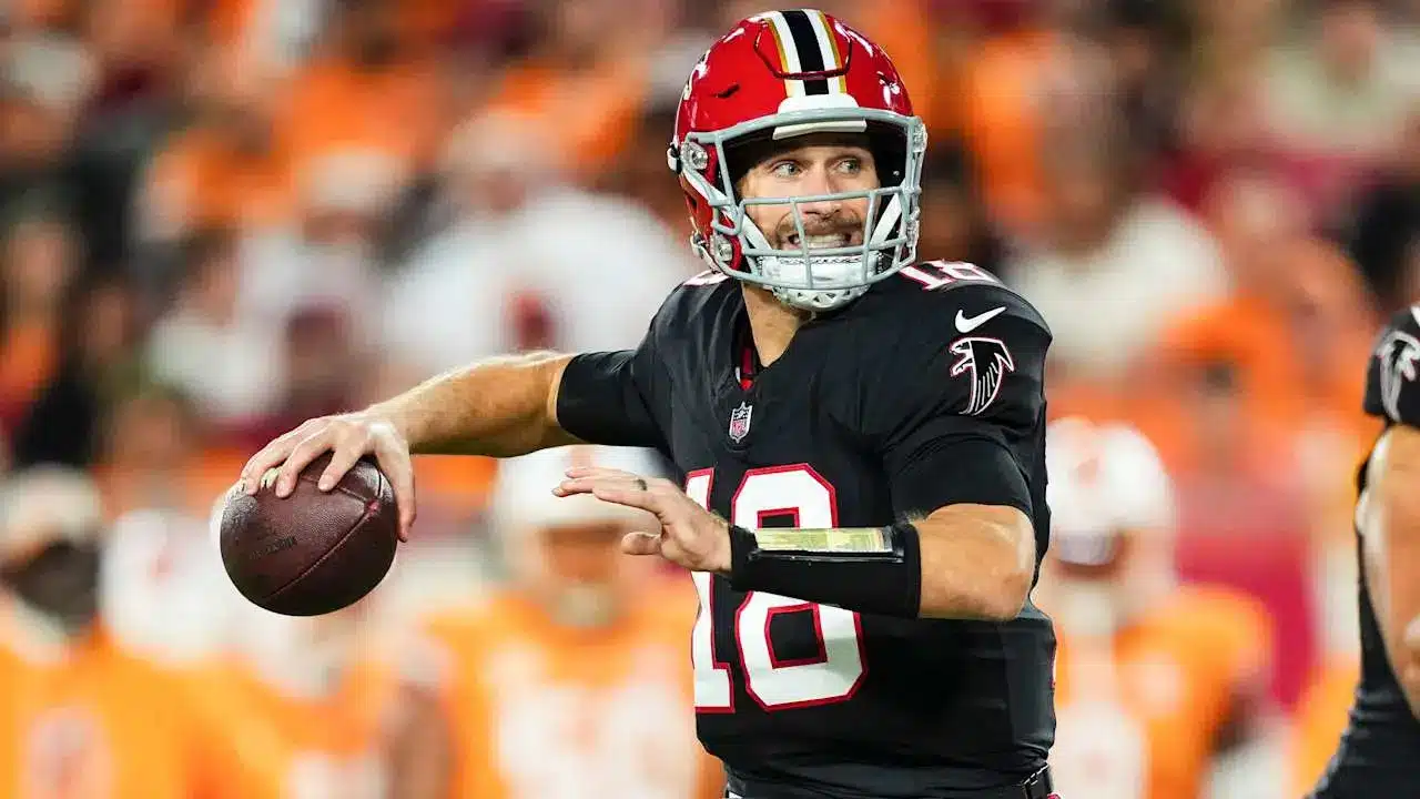 Kirk Cousins in a black Atlanta Falcons jersey and red helmet holding a football