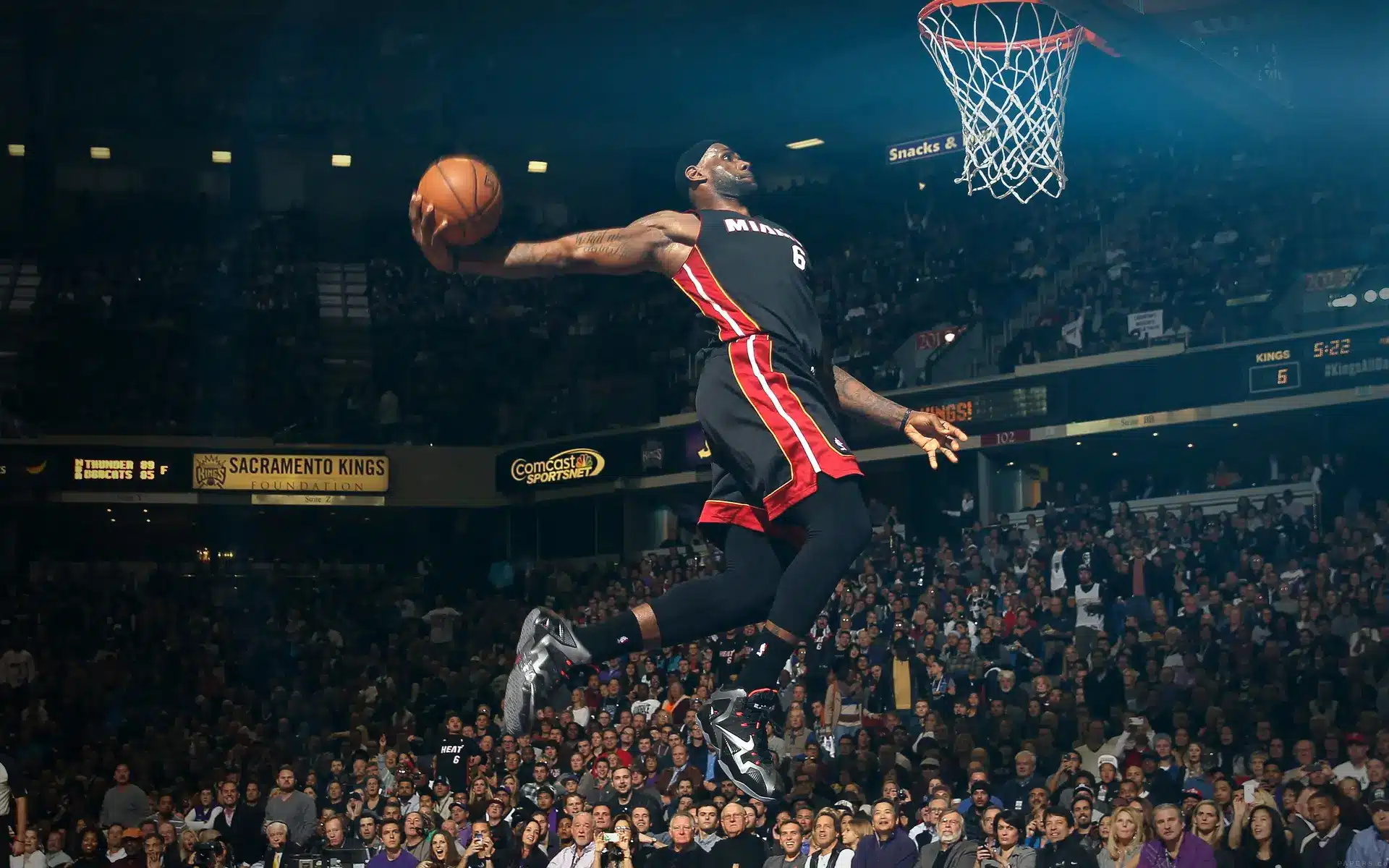 LeBron James in a black Miami Heat jersey leaping toward the hoop for a slam dunk