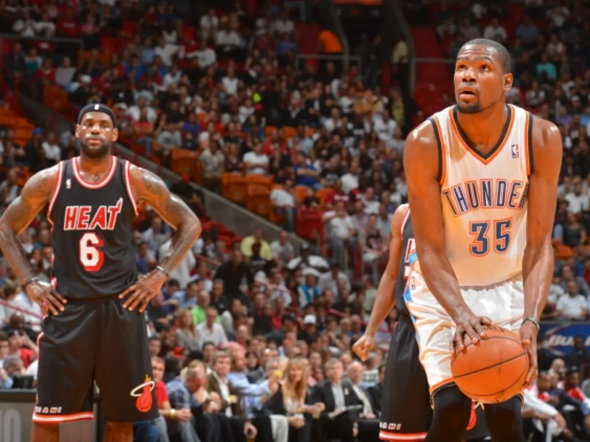Kevin Durant in a white Oklahoma City Thunder jersey holding a basketball with LeBron James in a black Miami Heat jersey