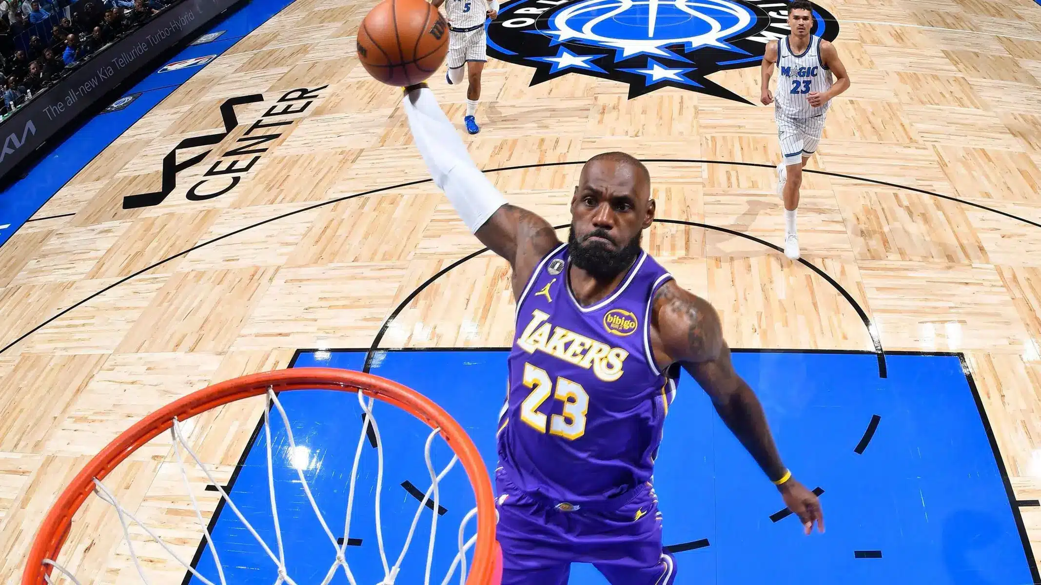 LeBron James in a purple Lakers jersey driving toward the hoop for a layup during an NBA game.