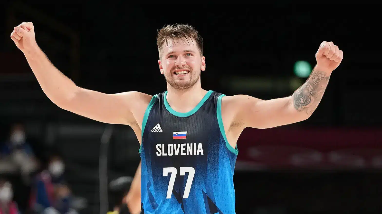 Luka Doncic wearing a blue Slovenia national team jersey with number 77, cheering with arms raised