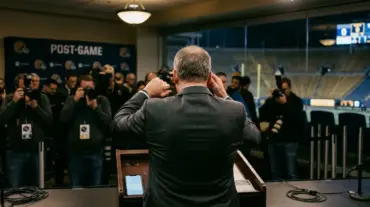 Frustrated football coach reacts during a tense postgame press conference after a shutout loss