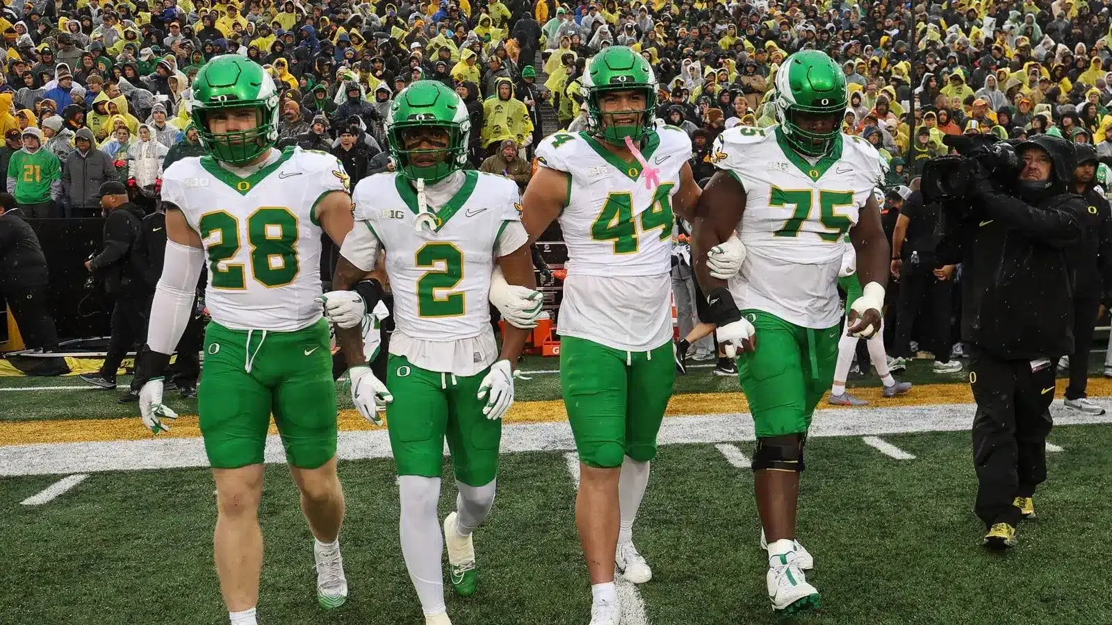 Four Oregon Ducks football players in white jerseys and green pants walking on the field during a game