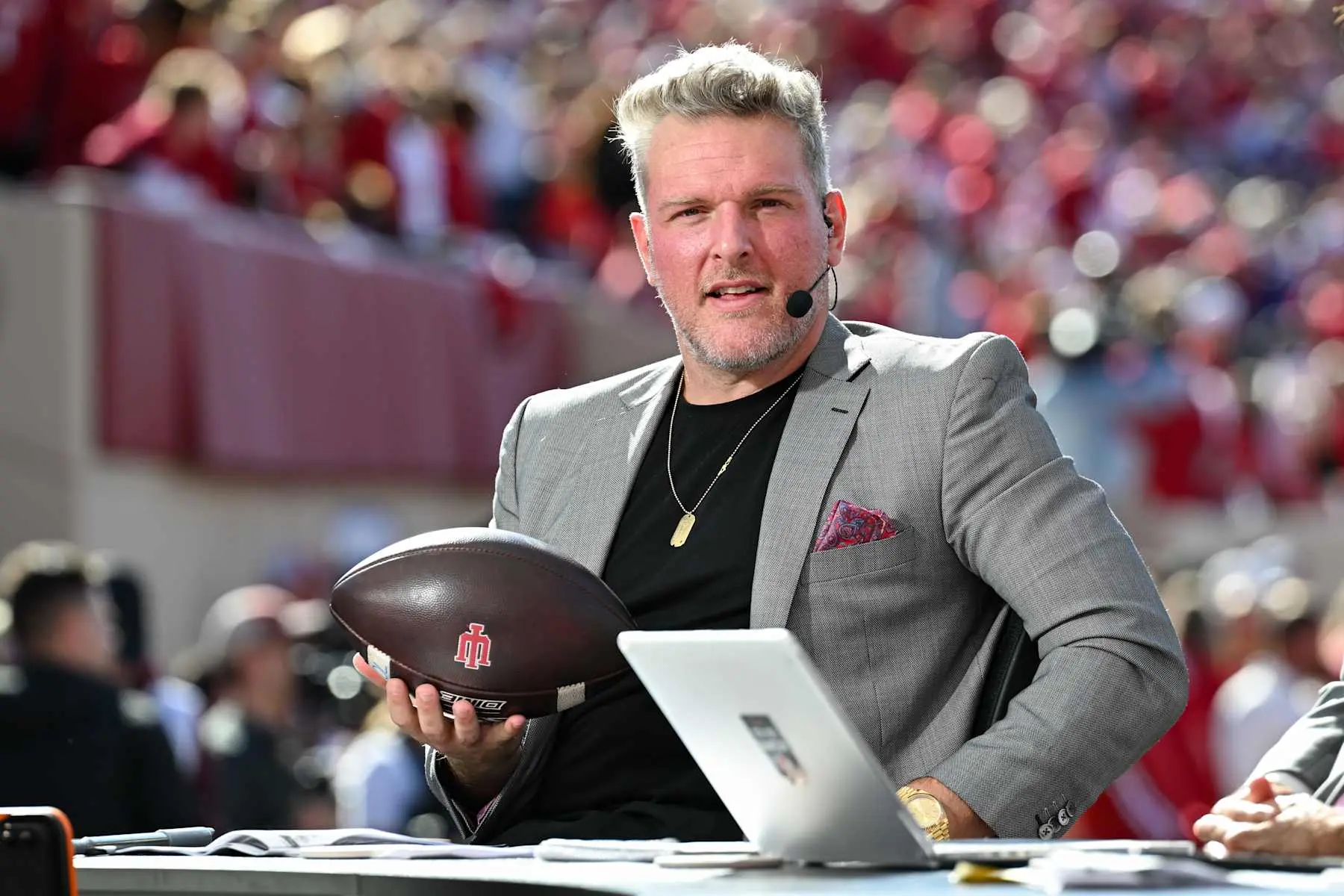Pat McAfee wearing a grey blazer and headset, holding an Indiana University football on College GameDay.