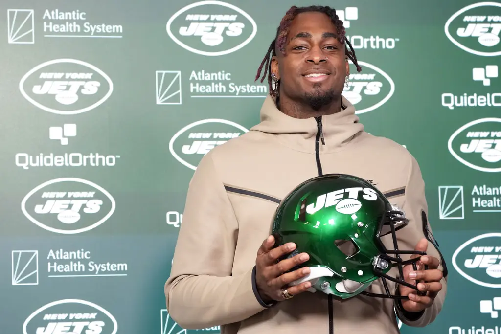 Will McDonald IV posing with a New York Jets helmet in front of a team backdrop